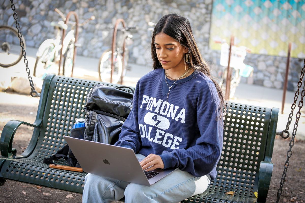 Student on laptop sitting on a bench.